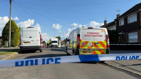 Police tape is seen across a road with a police forensics car on the scene