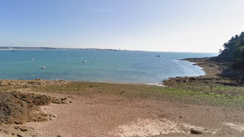 A sandy shoreline and sea water. Boats are in the water. The sky is blue.