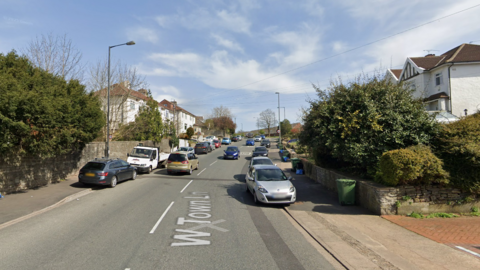 Google maps street view of West Town Lane in Brislington, Bristol. The street is steep and residential and there are houses on either side of the road. There are cars parked up on either side of the road.