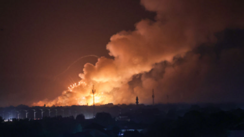 In the distance the sky is illuminated by fire and bellowing smoke after an ammunition dump in Chad's capital caught fire.