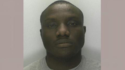 A mug shot of Segin Ogundipe. He is looking into the camera with a blank face and is wearing a light grey sweatshirt
