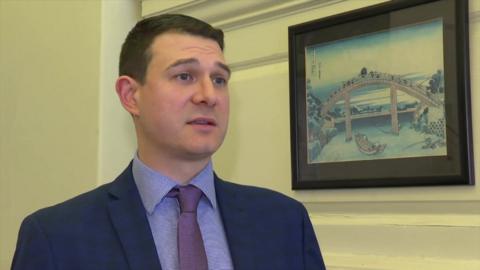 A man in a navy blazer, a blue shirt and purple tie. 