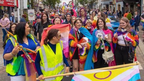 A crowd of people dressed in rainbow colors and holding flags celebrate the Pride festival in Omagh.
