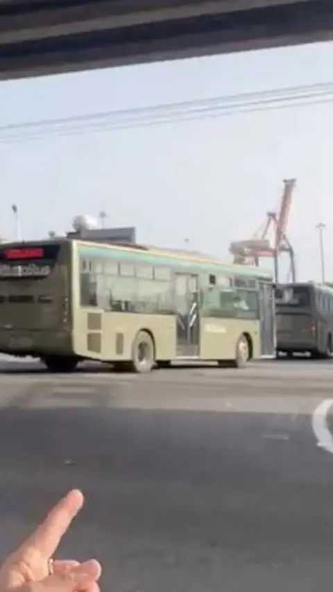 A hand pointing at military buses driving down a road
