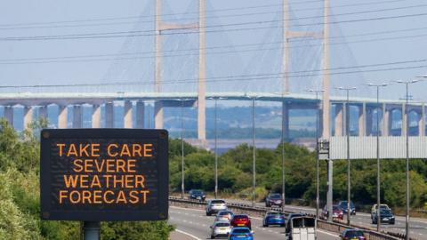 Traffic approaches the Severn Bridge with a road sign warning people: take care, severe weather forecast