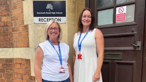 A photo of two women standing outside a front door with a reception sign on the wall next to them