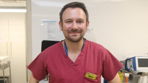 Alex Oliver in red scrubs in a hospital room.