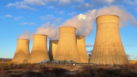 A view of Ratcliffe-on-Soar power station's cooling towers, which are billowing out steam on a sunny day.