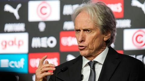 Jorge Jesus, wearing a black suit, gesticulates with his right hand while speaking at a press conference 