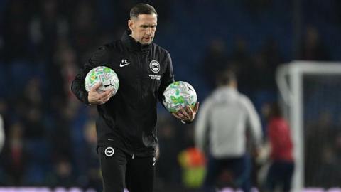 Andrew Crofts on the pitch holding two footballs before a Brighton game