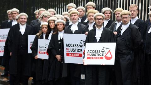 Lawyers dressed in their black robes and wigs standing outside court in Belfast holding signs saying access to justice.