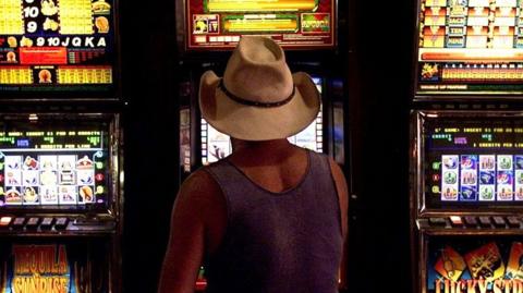 A man in a hat plays pokie machines