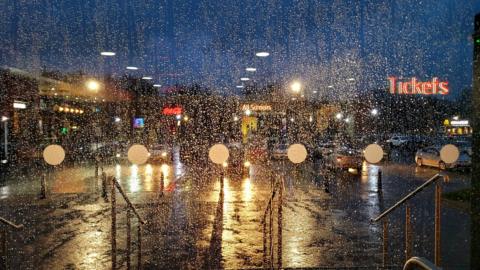 Window with raindrops. Dark evening sky with shops and city centre lights below. 