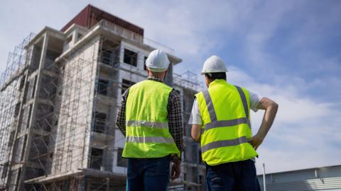 Two construction workers looking up at building under construction