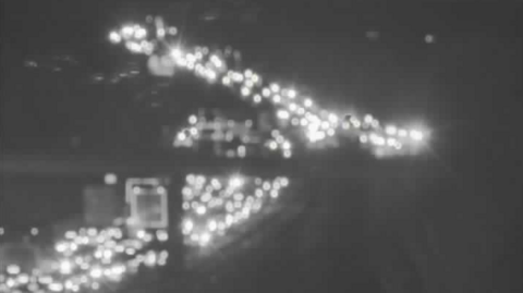 Grainy/black and white blurry image of lots of car lights on a congested M11 going under a bridge 