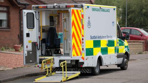 An ambulance sits outside a house waiting for patients - the back of the ambulance is open. 