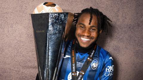 A smiling Ademola Lookman poses with the Europa League trophy, a winner's medal and the match ball