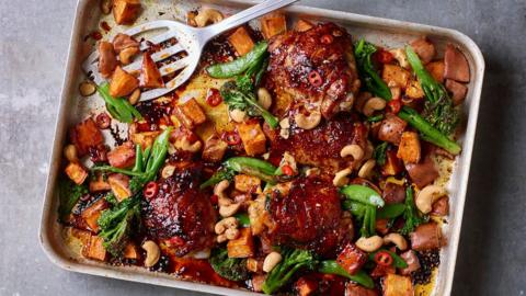 Sticky glazed orange chicken with greens and cubes of sweet potato in a silver oven tray,