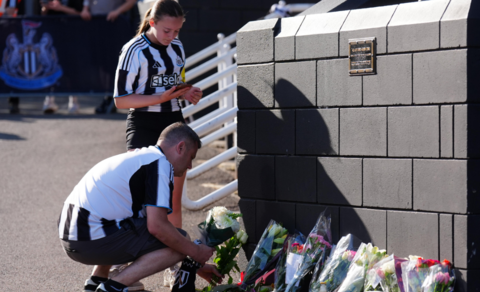 A man and a girl in Newcastle football jerseys lay flowers outside St James Park