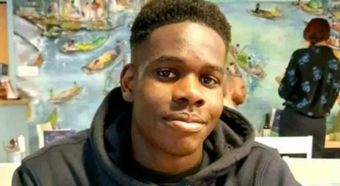 Young man with black hoodie and dark skin smiling softly at the camera