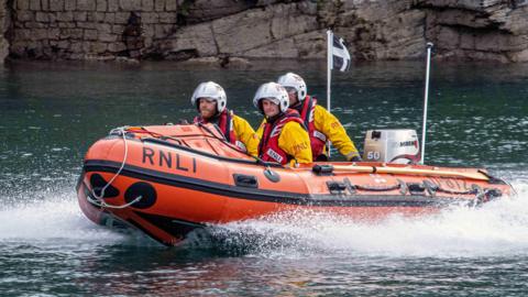 An orange rescue boat off the coast of Looe in Cornwall with the letters RNLI on the side.