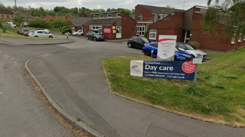 A Google maps image of a care home with small buildings and cars parked outside.