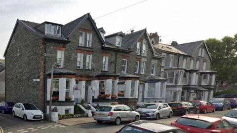 Harvington House in Keswick. The guest house is an end of terrace property with bay windows, dormer windows, slate cladding and white detailing. Every parking space on the street and a side street off it has been taken.