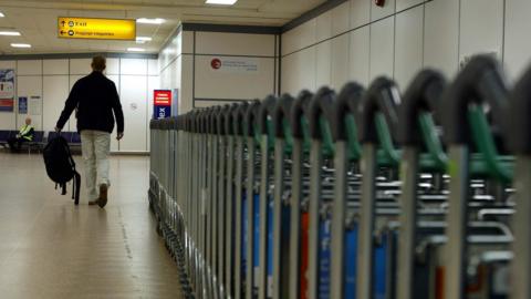 A man walks past luggage trollies at Gatwick Airport