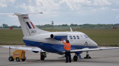 People in orange hi-vis jacket work on a small white aircraft in an airfield
