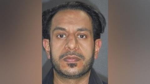 A police mugshot of Yasar Hussain, a man with black hair, a receding hairline, dark eyes and short stubble