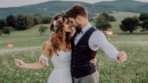 A man and a woman at their wedding holding sparklers in a field