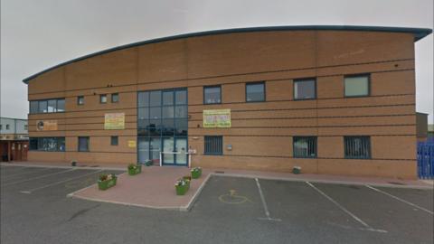 The outside of the nursery building. It is a large brick building with a curved roof and blue door and windows