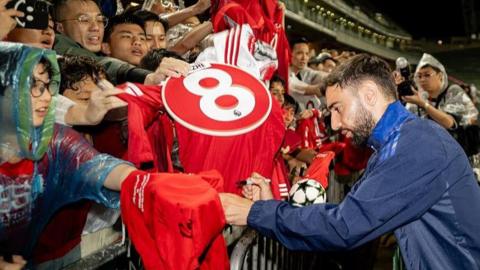Manchester United skipper Bruno Fernandes signs a shirt for a fan during a training session in Hong Kong