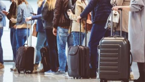 A queue of passengers with cabin baggage