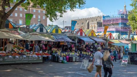 People walk past stalls selling fruit and veg and luggage at Norwich Market on Gentleman's Walk