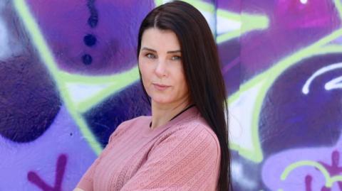 Amanda Cropper, owner of Flirtz strip club, stands in front of a wall of graffiti