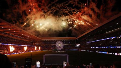 Three sides of Villa Park, with the pitch in darkness and the surrounds lit up with pyros and a tifo before a Champions League game