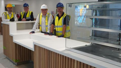 Four men in hard hats behind a new counter. The men are smiling at the camera.