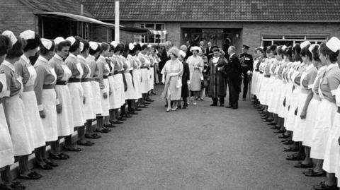 A black and white photograph showing Queen Elizabeth the Queen Mother, inspecting nurses.