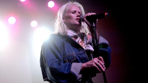 Lauren Bennett sings onstage during a concert. She wears a denim jacket