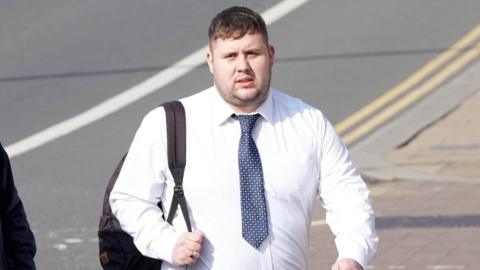 A man in a white shirt and blue tie with a backpack over his shoulder.