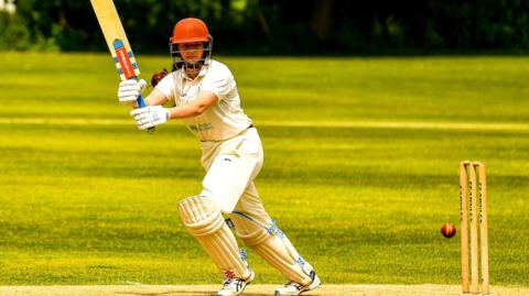 Libby, in University of Worcester kit hitting a square cut on her way to 179 not out in 30 overs against Swansea University at Ynystawe Cricket Club. Dressed in cricket whites with a red helmet and grill, her bat is held almost upright as she chops down on the ball