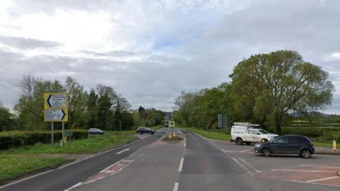 Lock's Garage junction shows the main A465 road, with roads going off in both directions to Abergavenny and Hay-on-Wye. There are white lines and chevron road markings and give way lines, as well as a bollard in the middle. Cars are crossing the junction in the Google Maps image.