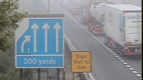 A motorway traffic camera showiing a single line of heavy traffic.
