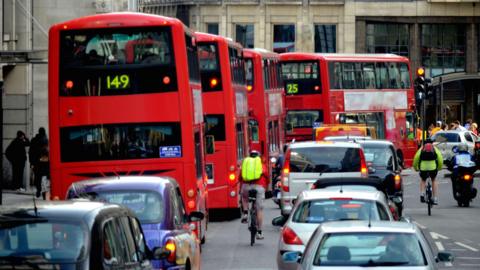 A row of red London buses among rows of cars and cyclists on a congested road in the City of London. 