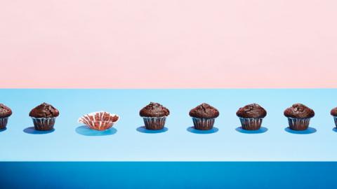 Chocolate muffins in a row with one eaten. On a pale blue and pink background