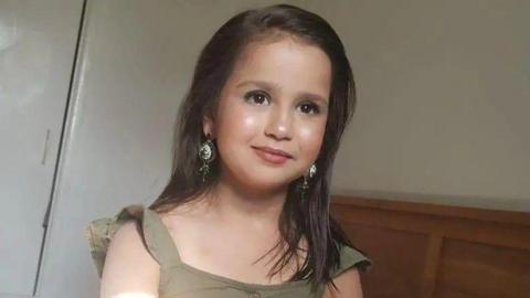 10-year-old Sara Sharif smiling. She is looking off to the right and wearing a green top