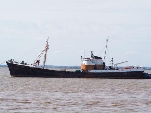 A large ship in water. It has two masts. It is black with a white and brown bridge. There is land in the distance.