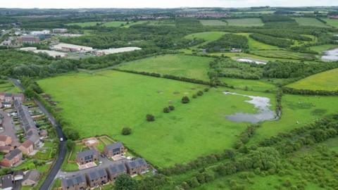 An aerial view of the meadows and fields next to a row of houses.