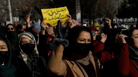 A woman with her face covered holds her hand up in a crowd of other women